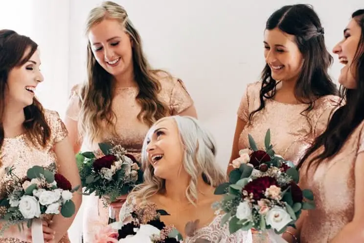 bridesmaids with flowers surrounding the bride and laughing