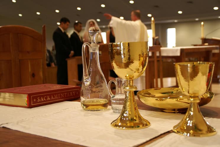 Catholic couple and priest in background to holy cup