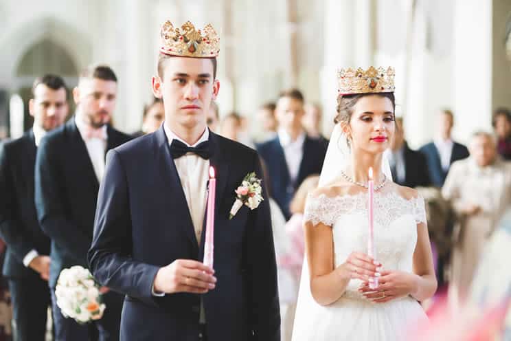 Orthodox wedding couple wearing Stefana crowns and holding candles