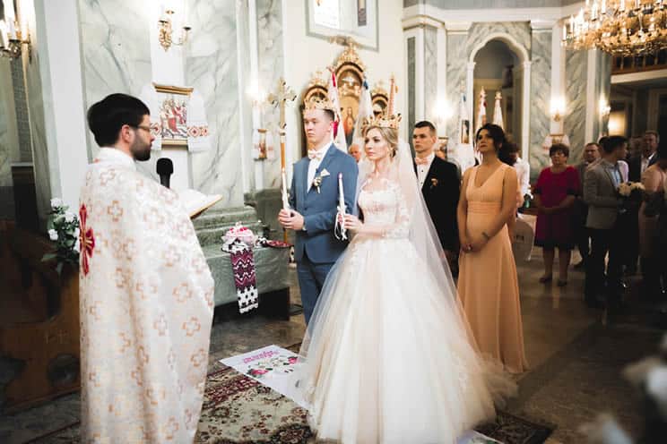 Orthodox wedding couple wearing Stefana crowns and carrying candles